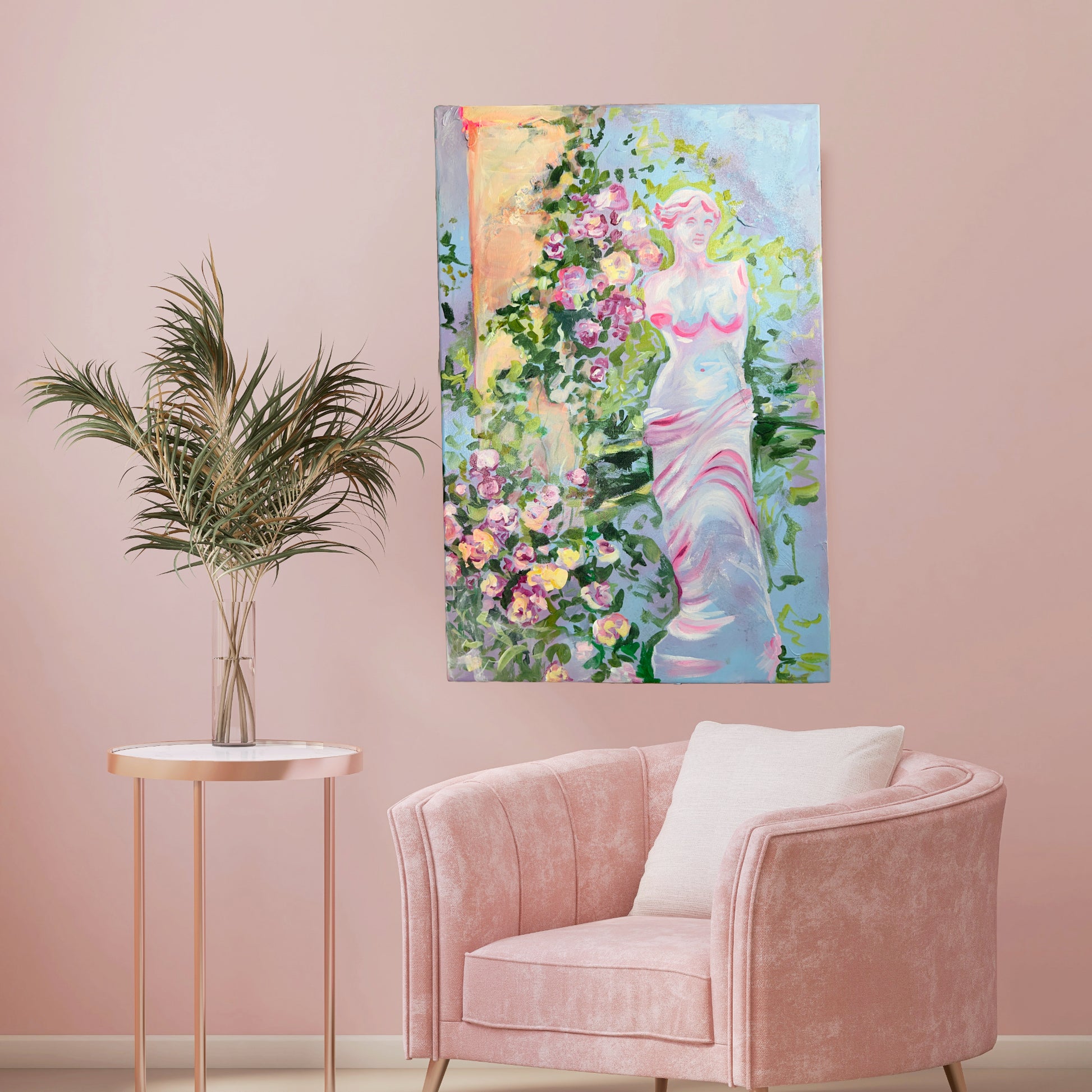 Original painting titled 'Garden Statue with Blooming Roses' by Natalie Zoghby displayed on a soft pink wall above a plush pink chair and a small side table with a decorative plant. The artwork, featuring a classical statue surrounded by vibrant roses, adds an elegant and serene touch to the modern, pastel-colored living room.